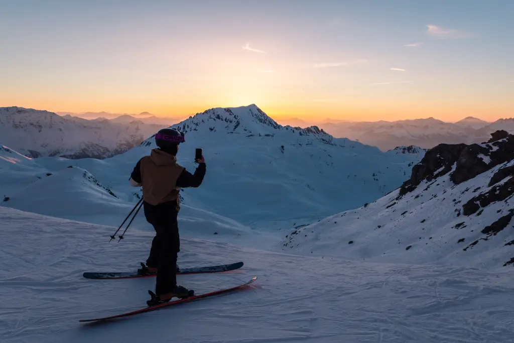 skieur qui prend en photo le coucher de soleil sur les pistes
