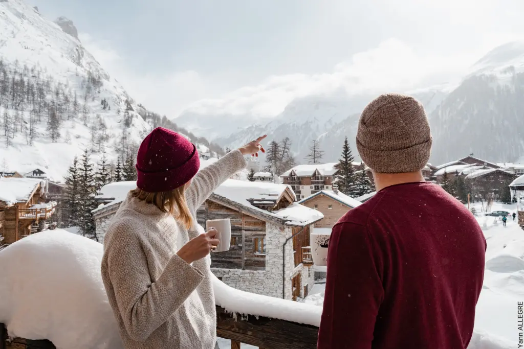 couple sur un balcon buvant un chocolat chaud et admirant le village de val d'isère en savoie
