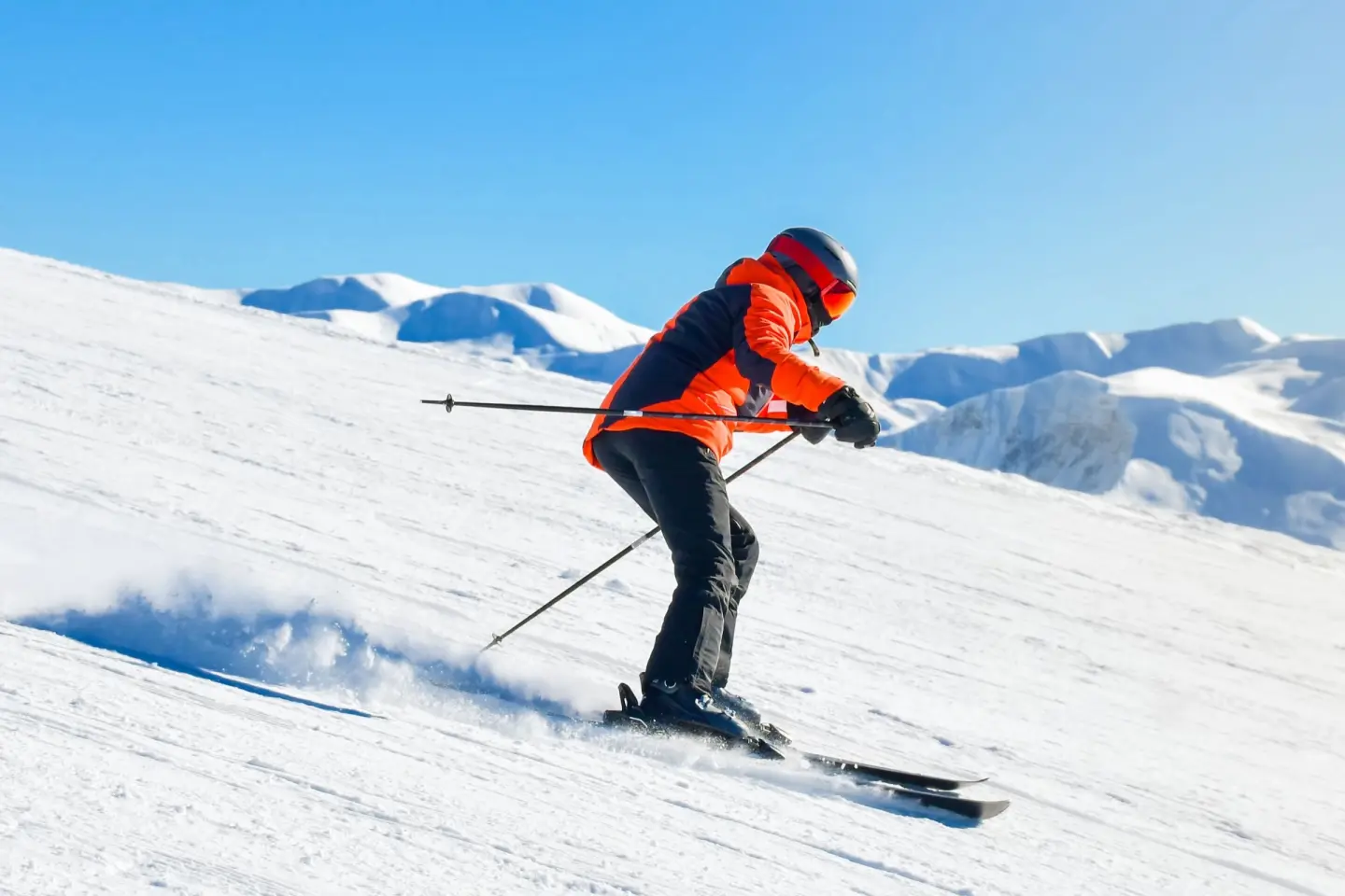 Un skieur en veste orange descend une piste damée sous un ciel bleu