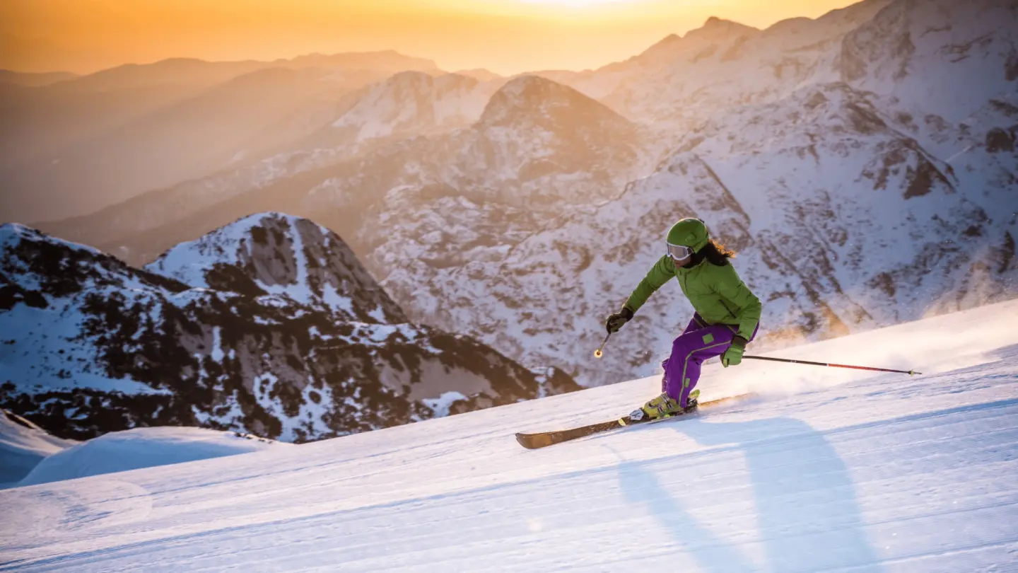 Une skieuse descend une piste au coucher du soleil