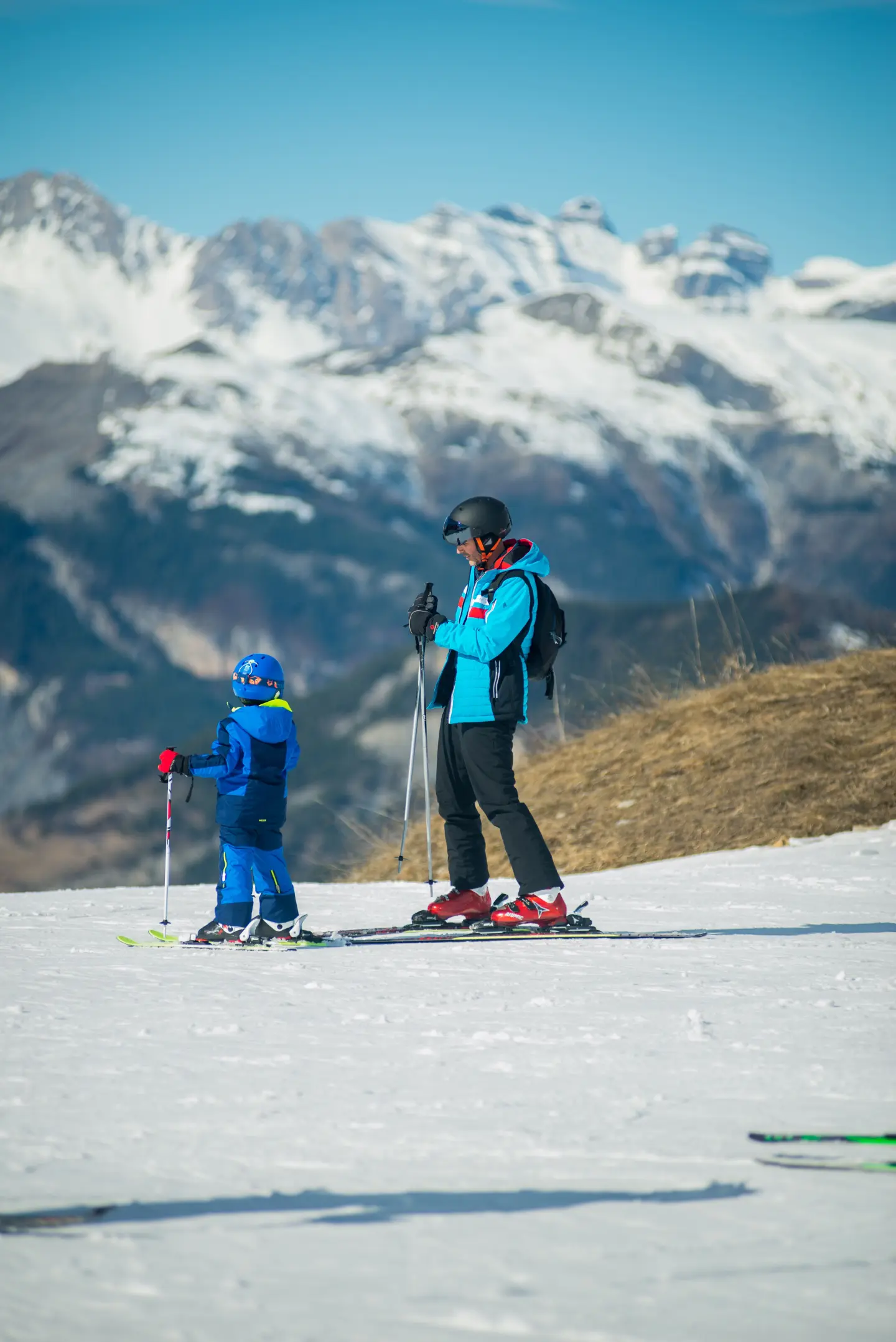 un père et son enfant en tenue de ski sur une piste de ski