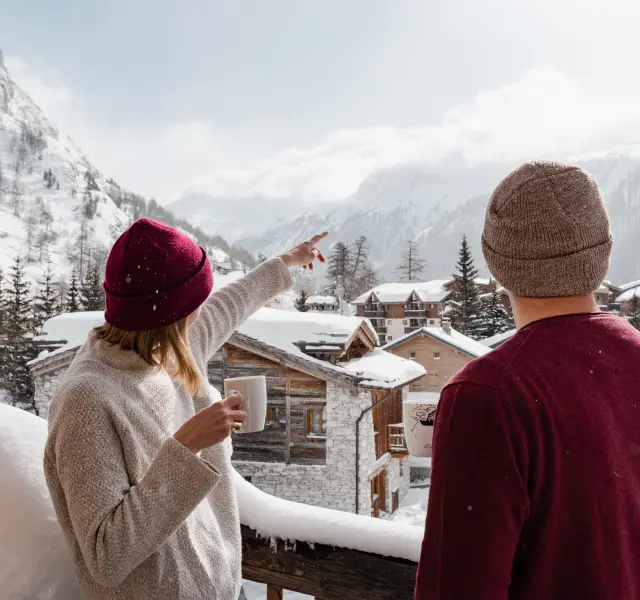 couple sur un balcon buvant un chocolat chaud et admirant le village de val d'isère en savoie