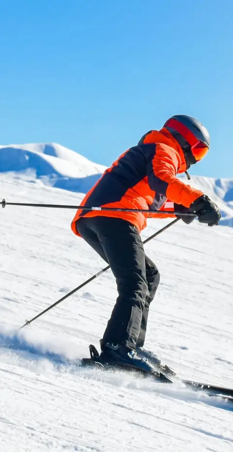 Un skieur en veste orange descend une piste damée sous un ciel bleu